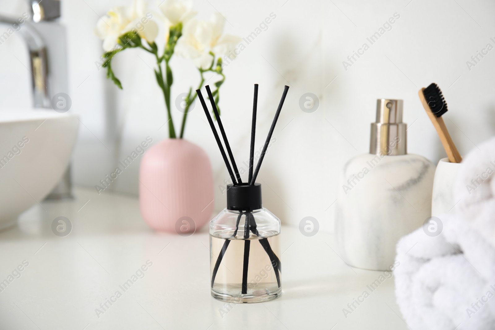 Photo of Aromatic reed air freshener, toiletries and flowers on white countertop in bathroom