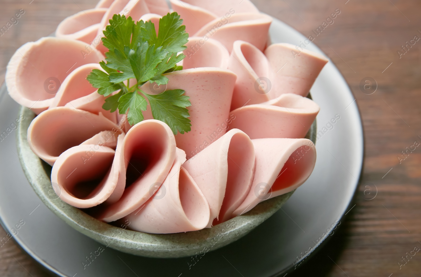 Photo of Slices of delicious boiled sausage with parsley on wooden table, above view