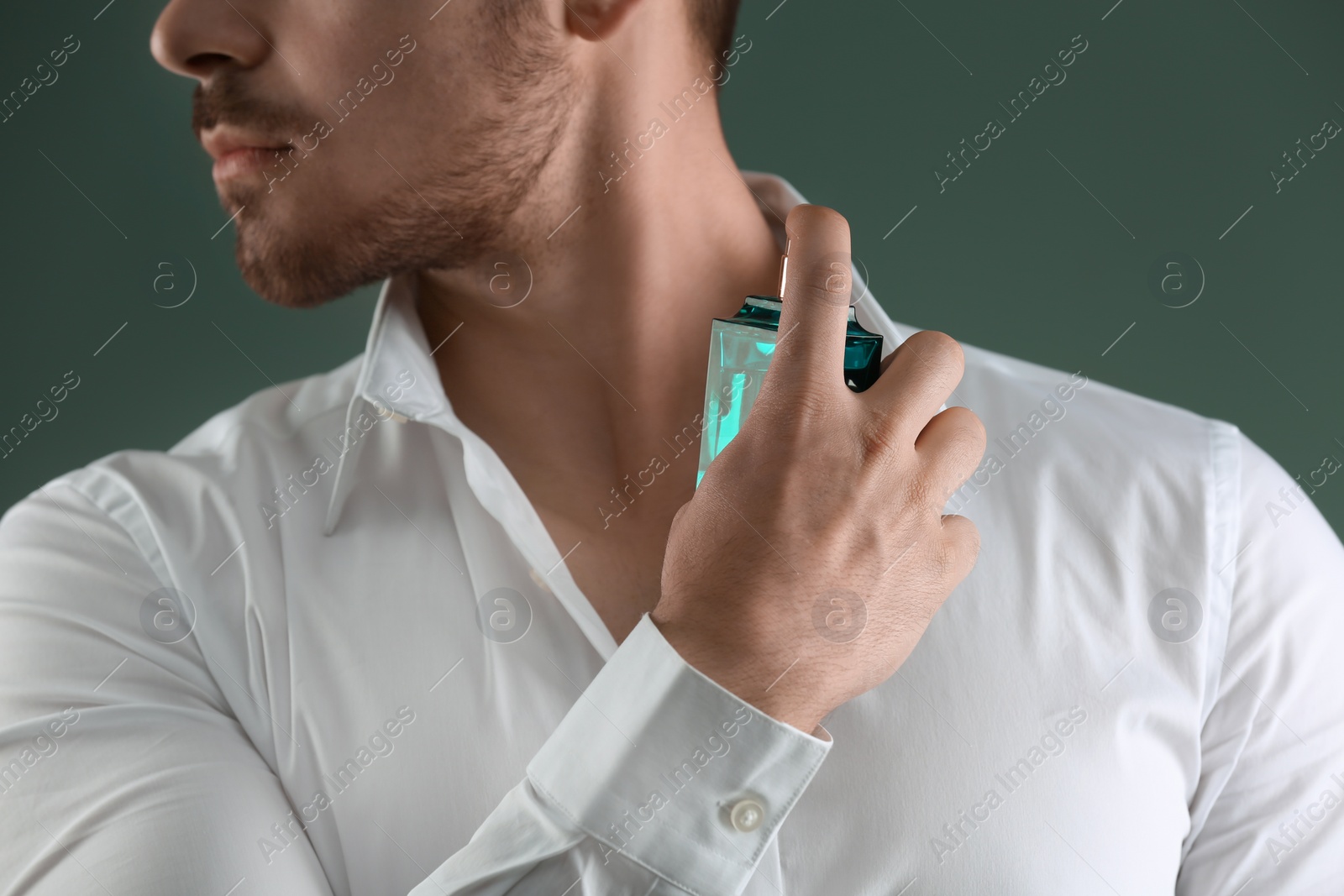 Photo of Handsome man in shirt using perfume on dark background, closeup