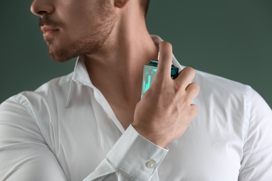 Photo of Handsome man in shirt using perfume on dark background, closeup