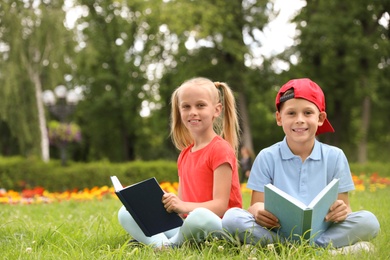 Photo of Cute little children reading books on green grass in park