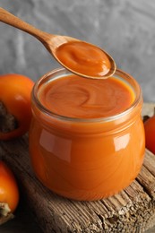 Photo of Spoon with delicious persimmon jam over jar, closeup