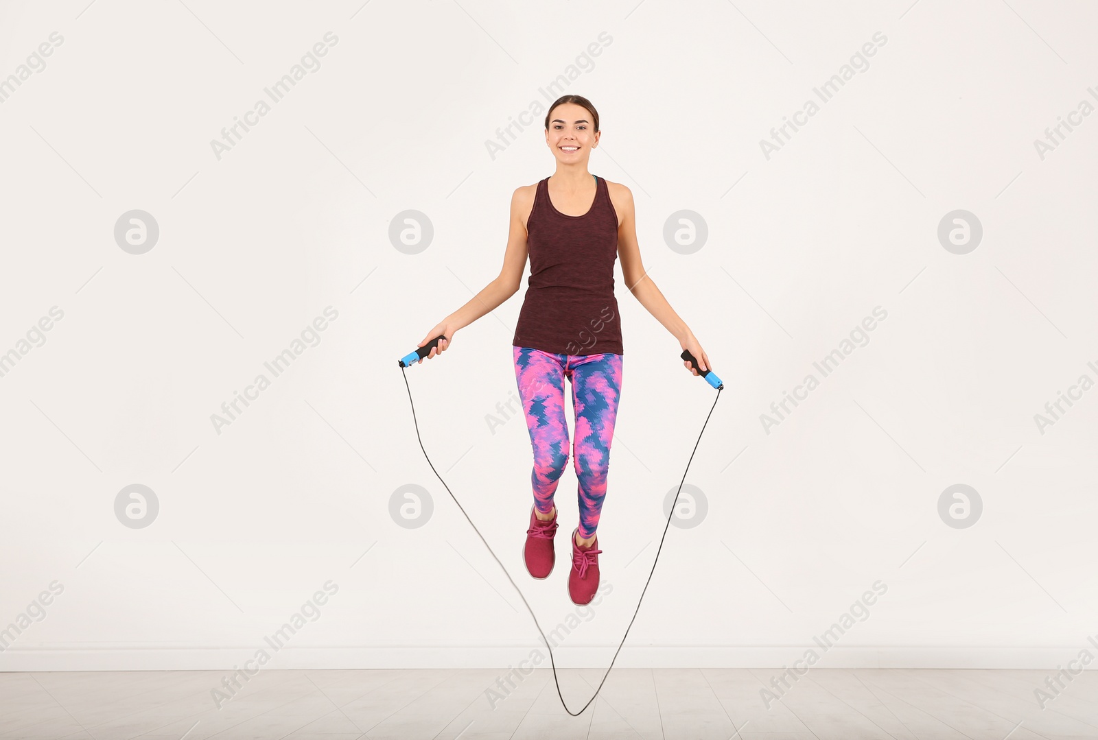 Photo of Full length portrait of young sportive woman training with jump rope in light room