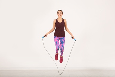 Photo of Full length portrait of young sportive woman training with jump rope in light room