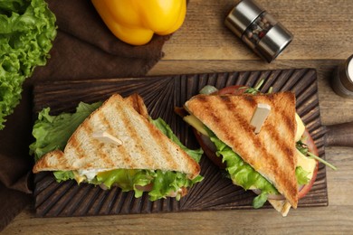 Wooden board with tasty sandwiches on table, flat lay