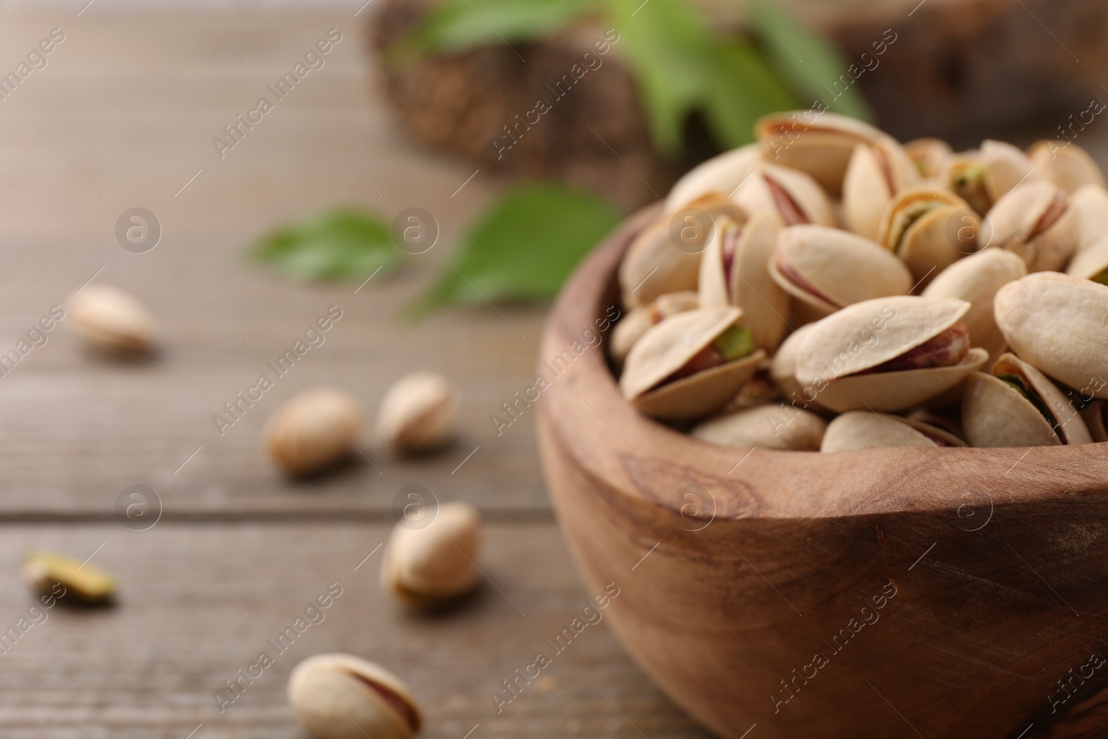 Photo of Tasty pistachios in bowl on wooden table, closeup. Space for text