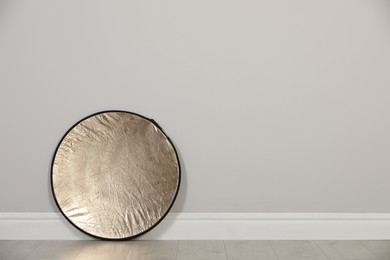 Photo of Studio reflector near grey wall in room, space for text. Professional photographer's equipment