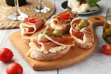 Photo of Tasty sandwiches with cured ham, tomatoes and olives on tiled table, closeup