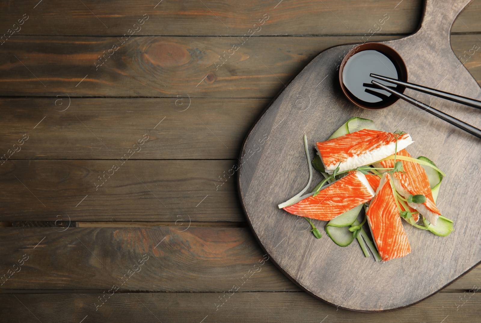 Photo of Fresh crab sticks with cucumber and soy sauce served on wooden table, flat lay. Space for text