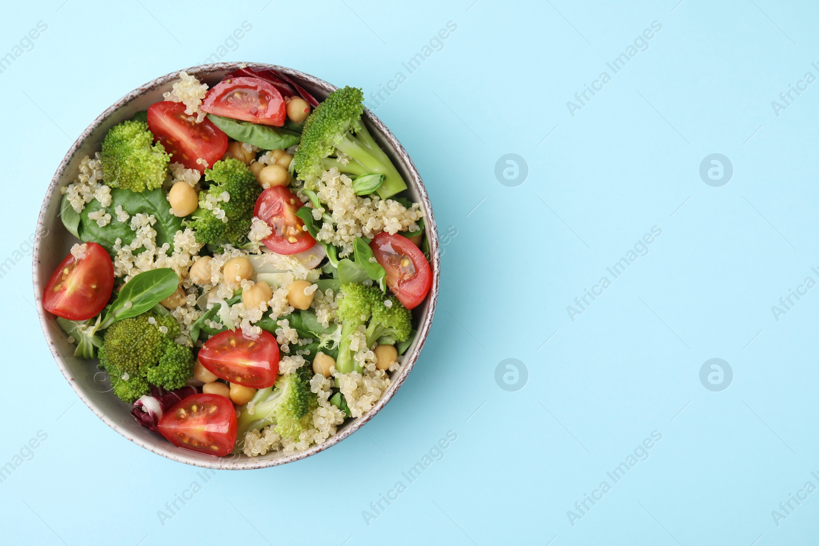 Photo of Healthy meal. Tasty salad with quinoa, chickpeas and vegetables on light blue table, top view with space for text