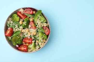 Photo of Healthy meal. Tasty salad with quinoa, chickpeas and vegetables on light blue table, top view with space for text