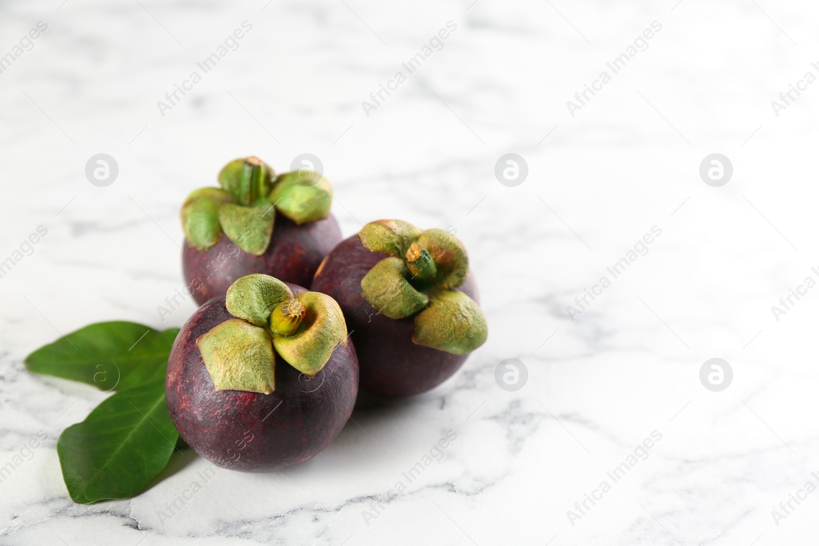 Photo of Fresh ripe mangosteen fruits on white marble table. Space for text