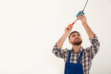 Photo of Electrician with screwdriver repairing ceiling lamp against white background