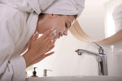Beautiful teenage girl washing face with cleansing foam in bathroom. Skin care cosmetic