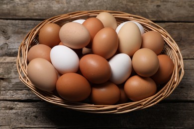 Photo of Fresh chicken eggs in wicker basket on wooden table, above view