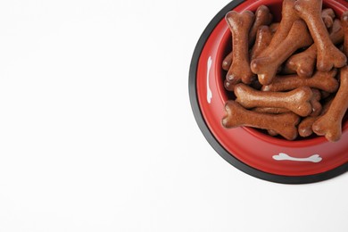 Photo of Red bowl with bone shaped dog cookies on white background, above view. Space for text