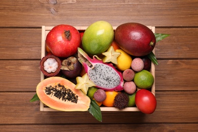 Crate with different exotic fruits on wooden table, top view