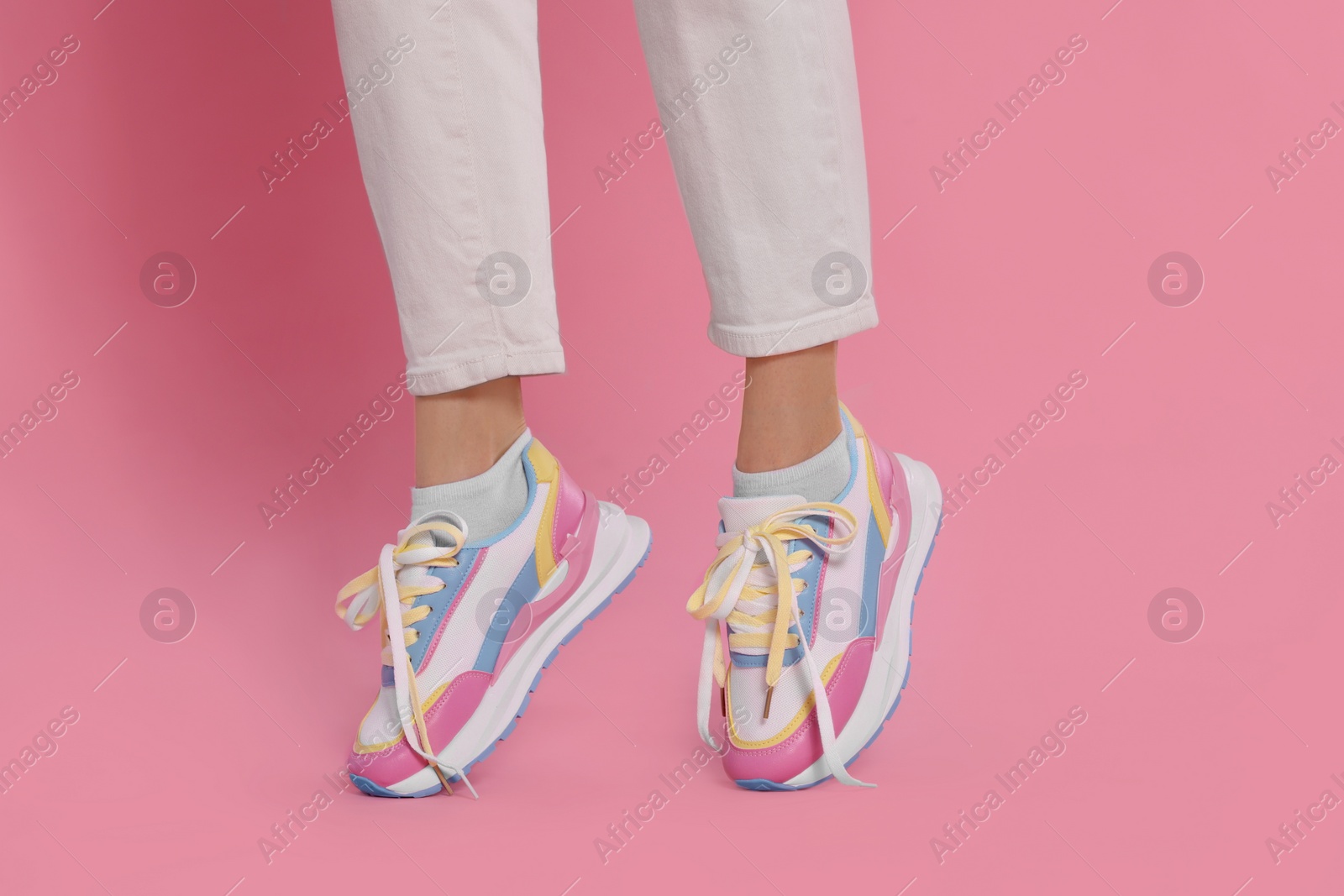 Photo of Woman wearing pair of new stylish sneakers on pink background, closeup