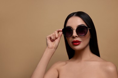 Photo of Attractive woman wearing fashionable sunglasses against beige background. Space for text