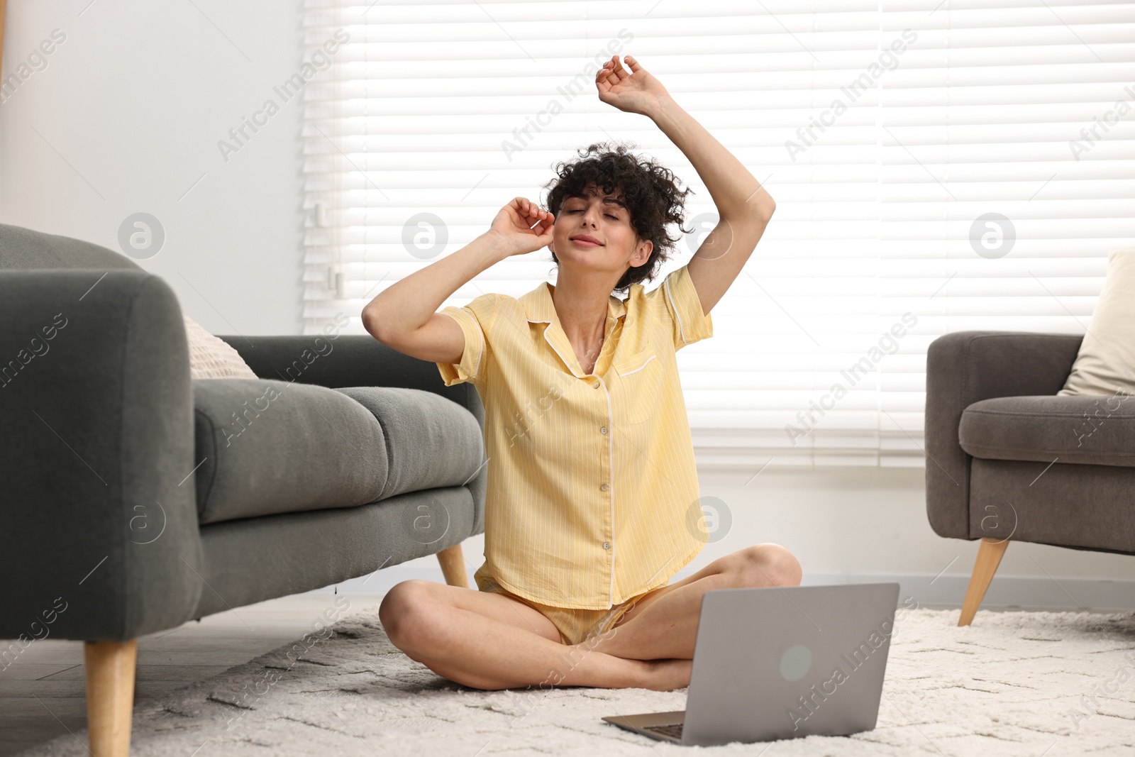 Photo of Beautiful young woman in stylish pyjama with laptop on floor at home