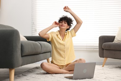 Photo of Beautiful young woman in stylish pyjama with laptop on floor at home