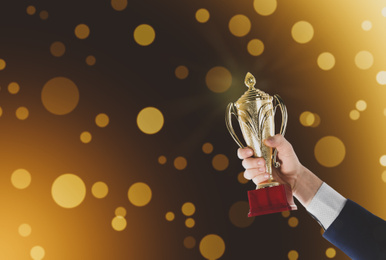 Businessman holding gold trophy cup on color background, closeup. Space for text