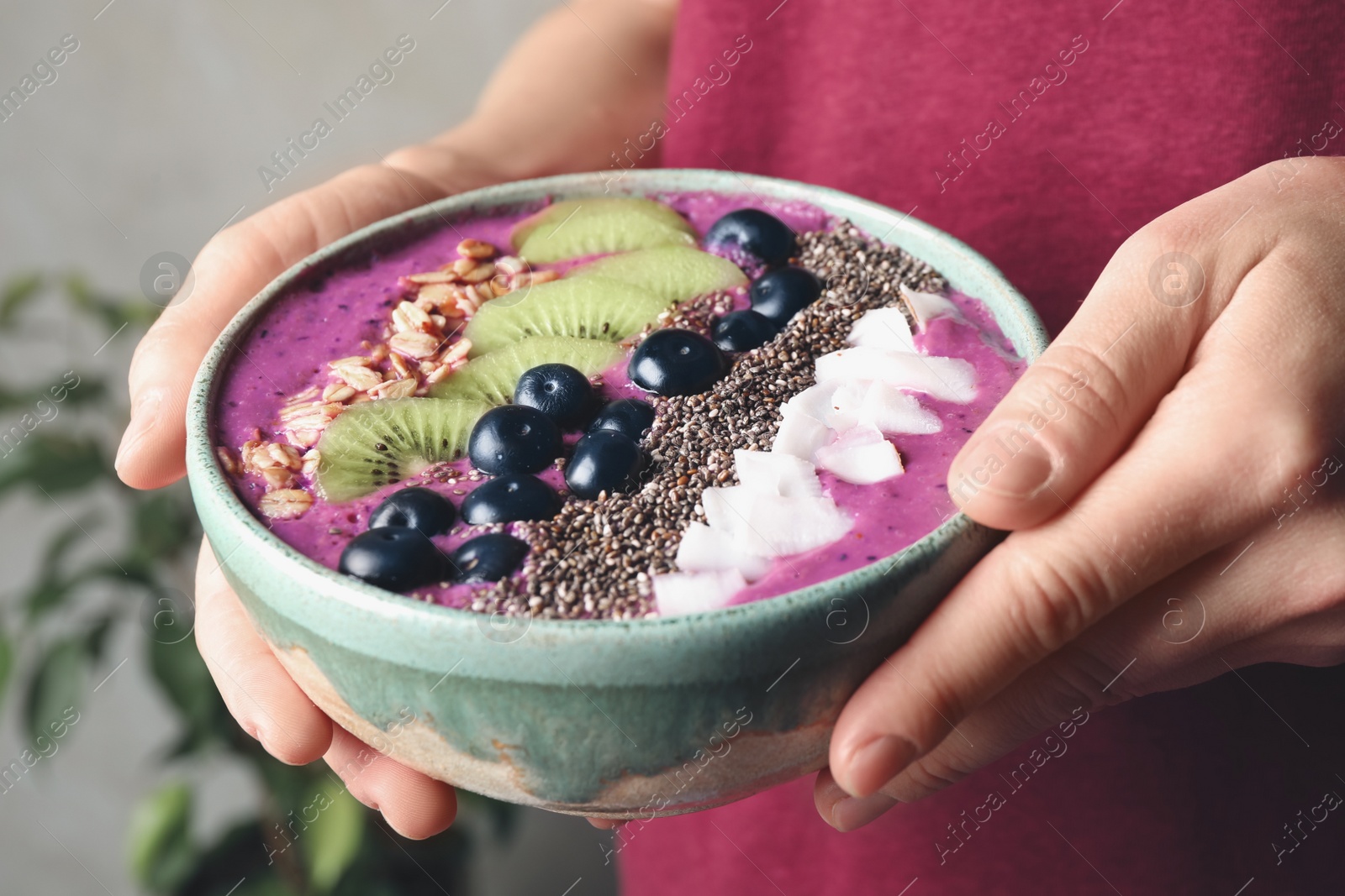 Photo of Woman holding bowl with tasty acai smoothie and fruits on blurred background, closeup