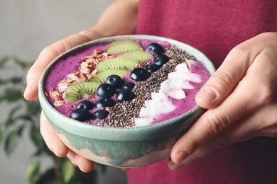 Woman holding bowl with tasty acai smoothie and fruits on blurred background, closeup