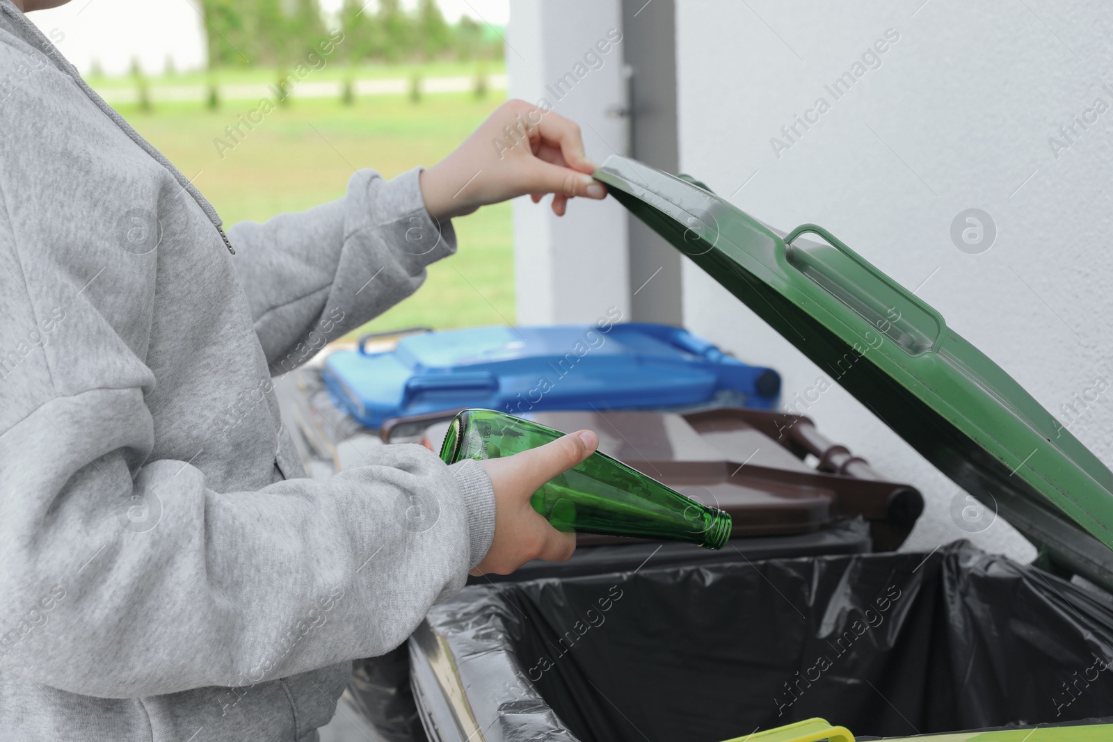 Photo of Woman throwing glass bottle in bin outdoors, closeup. Recycling concept