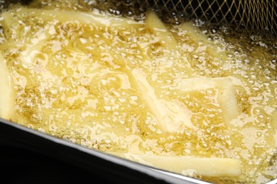 Photo of Cooking delicious french fries in hot oil, closeup