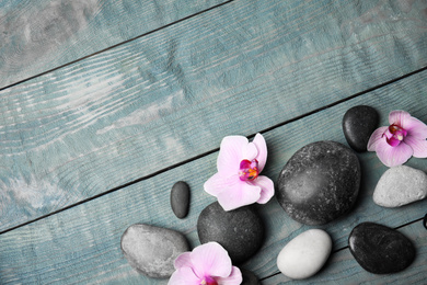 Photo of Stones with orchid flowers and space for text on blue wooden background, flat lay. Zen lifestyle