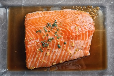 Raw salmon fillet with marinade in baking dish on table