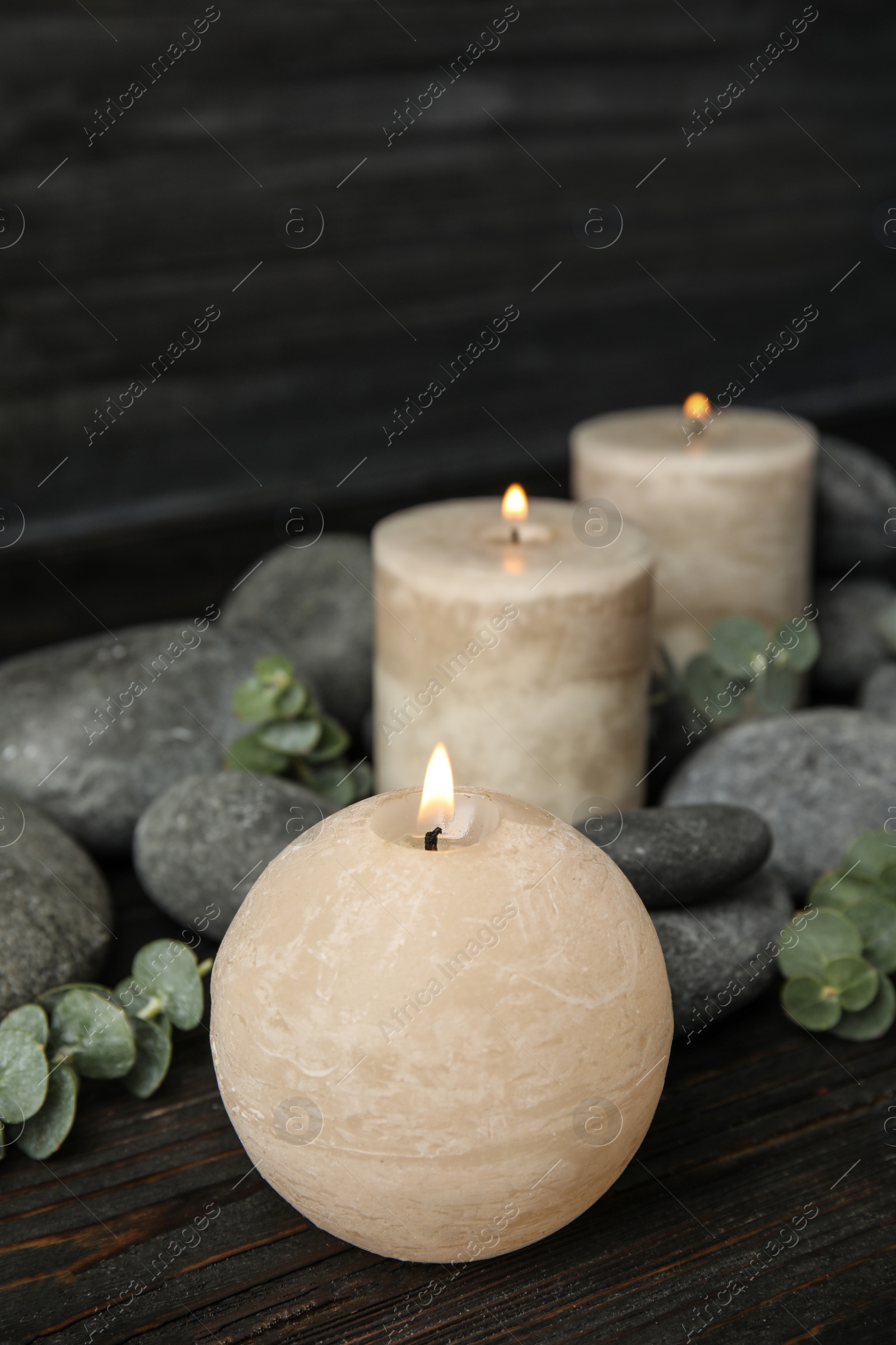 Photo of Composition with burning candles, spa stones and eucalyptus on dark wooden table, space for text