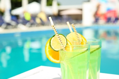 Refreshing cocktail in glasses near outdoor swimming pool on sunny day. Space for text