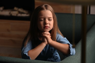Photo of Cute little girl with hands clasped together praying at home