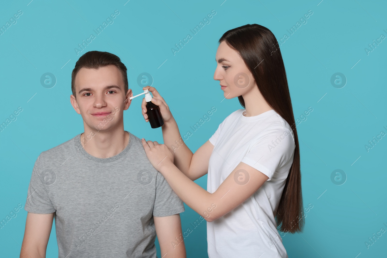 Photo of Woman spraying medication into man's ear on light blue background