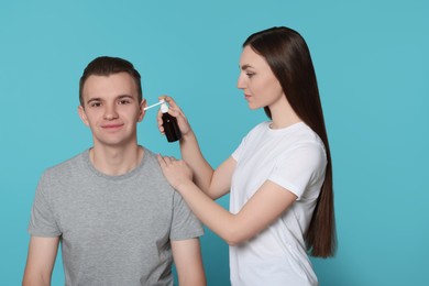 Woman spraying medication into man's ear on light blue background