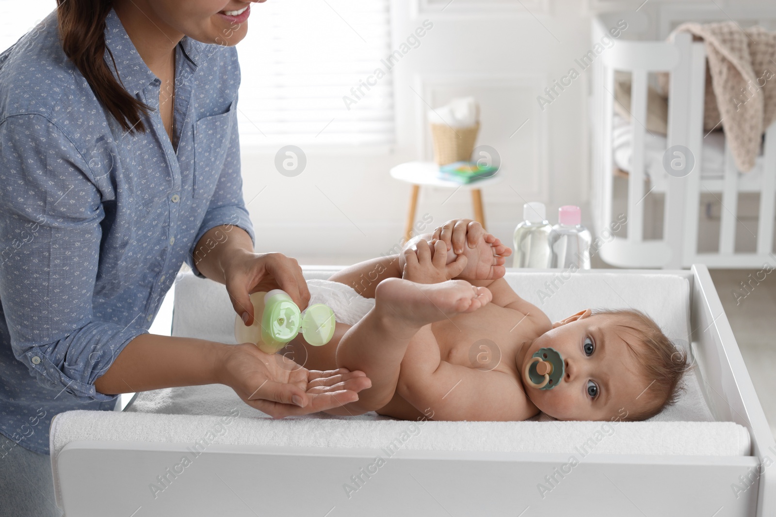 Photo of Mother with bottle of massage oil near baby on changing table at home, closeup