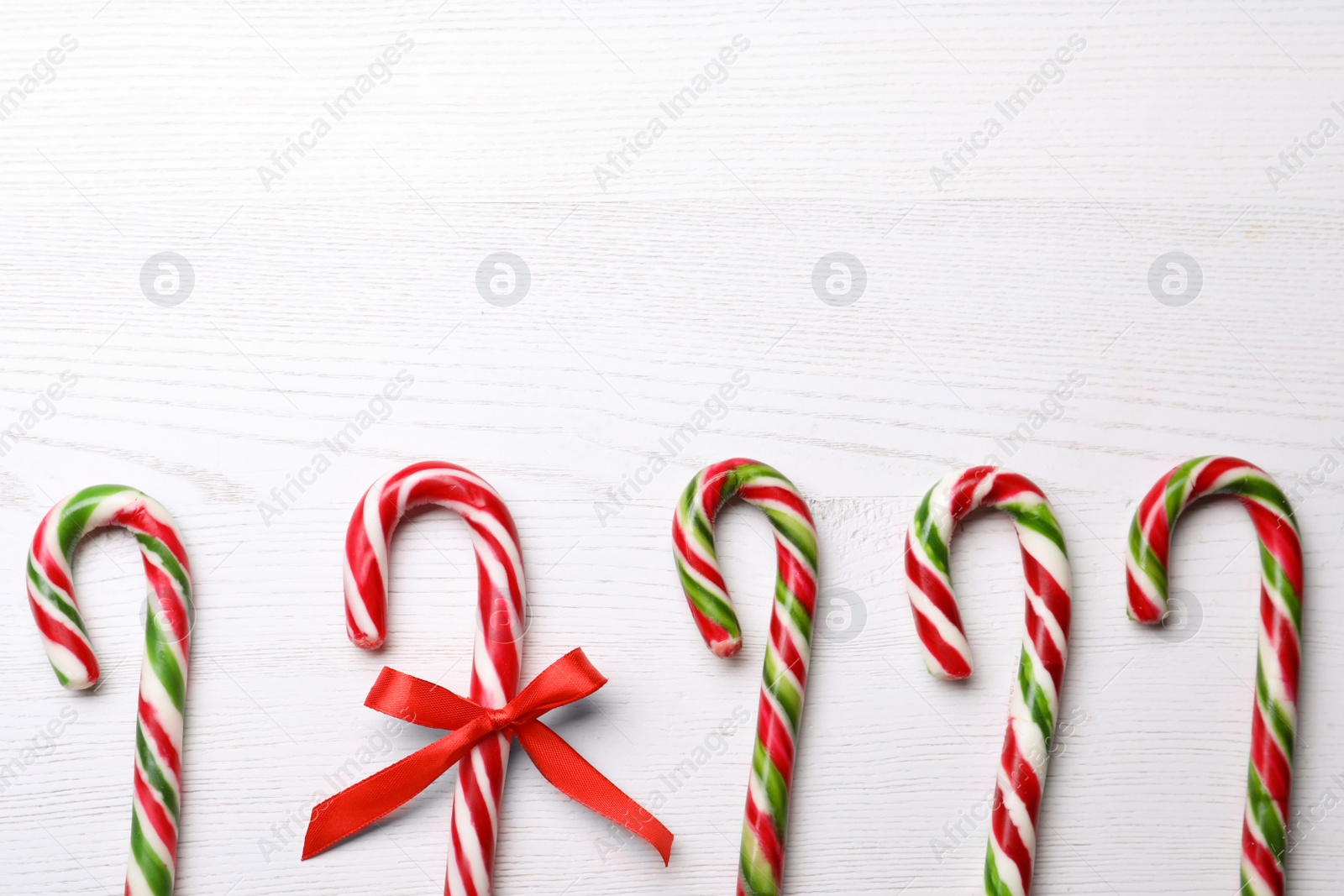 Photo of Sweet Christmas candy canes and one with bow on white wooden table, flat lay. Space for text