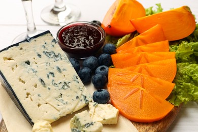 Photo of Delicious persimmon, blue cheese, blueberries and jam served on white wooden table, closeup