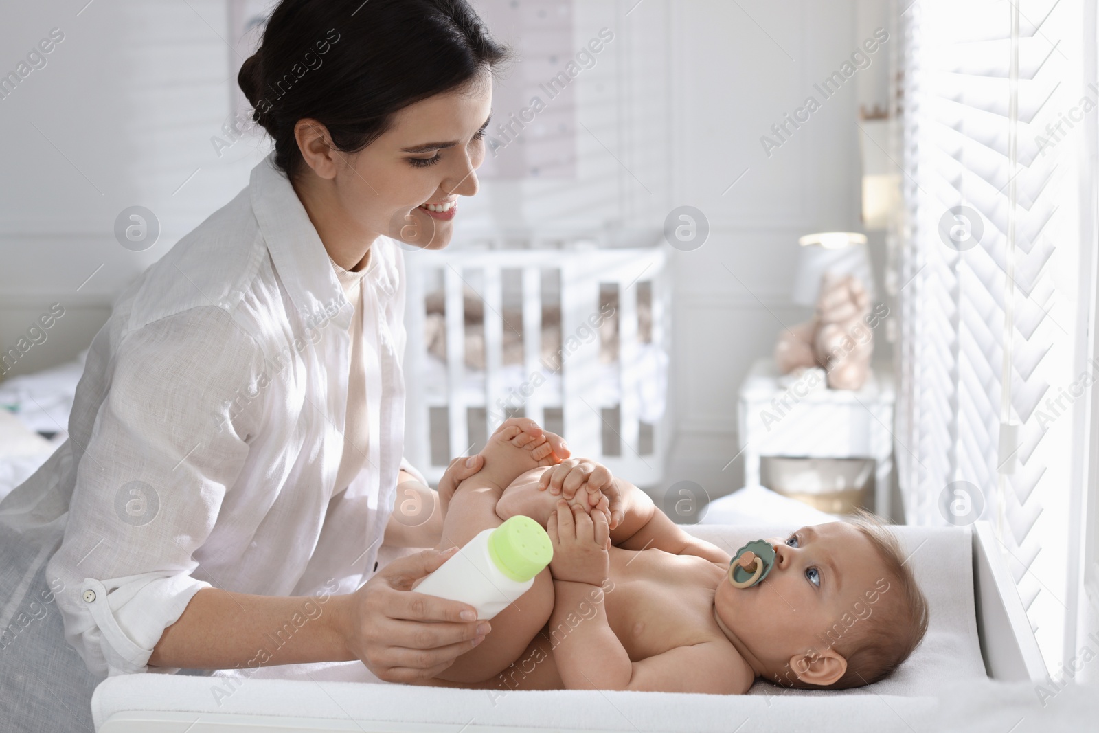 Photo of Mother with bottle of dusting powder near her cute baby at home