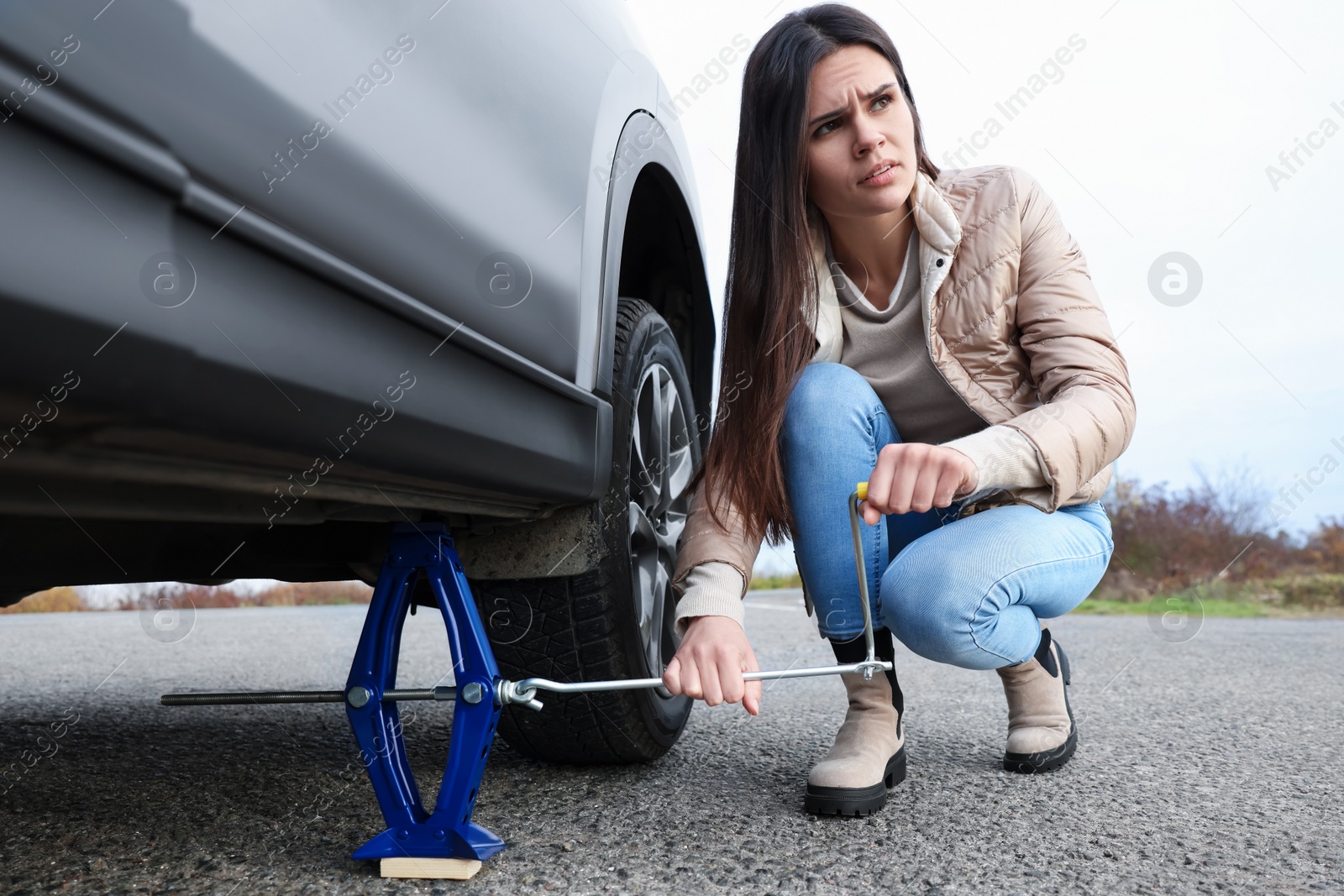 Photo of Young woman changing tire of car on roadside