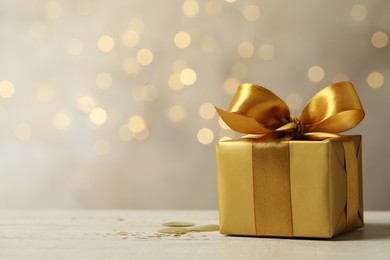 Photo of Beautiful golden gift box on light table against blurred festive lights, space for text