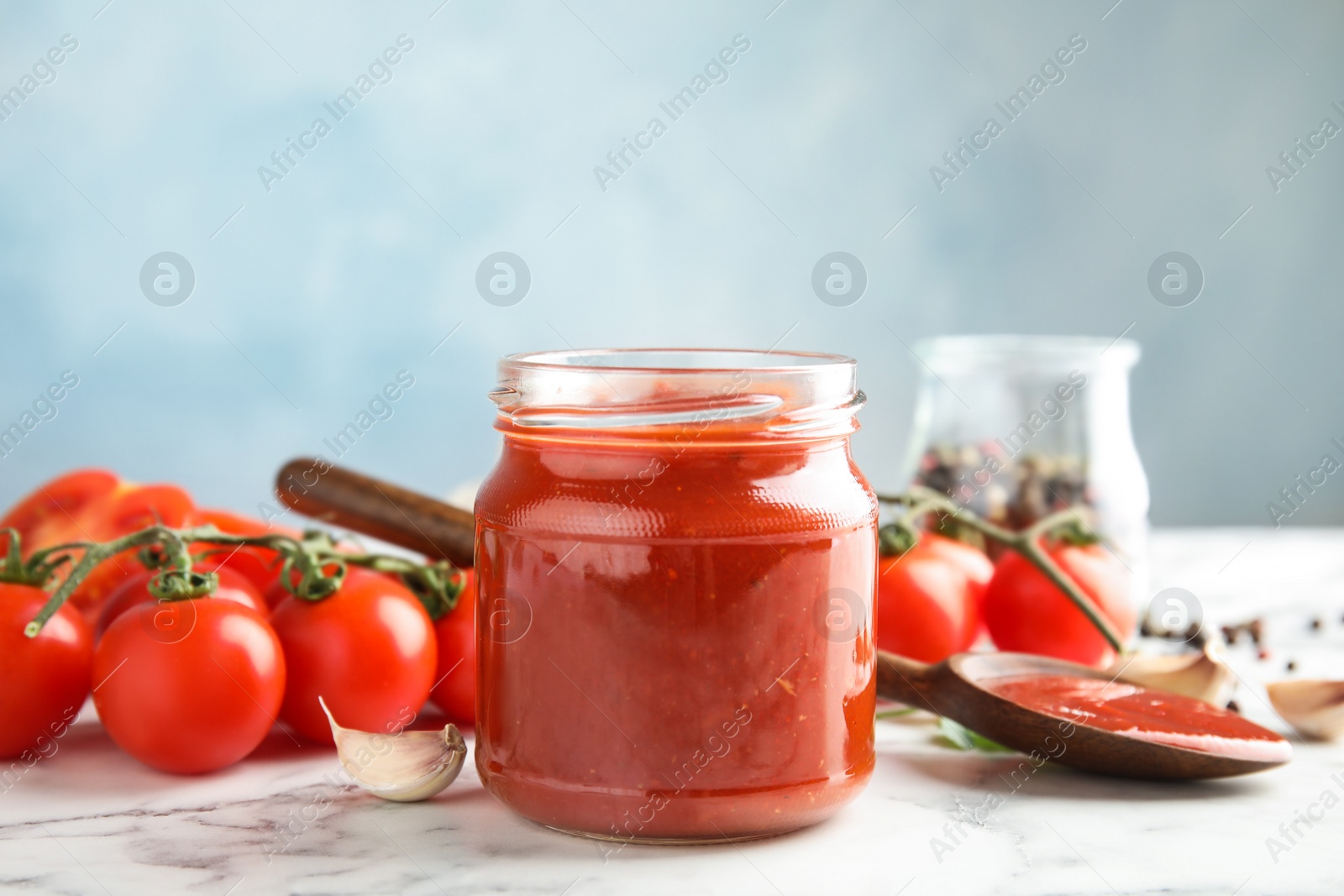 Photo of Composition with jar of tasty tomato sauce on table against color background