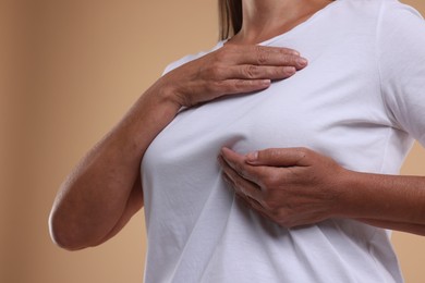 Photo of Woman doing breast self-examination on light brown background, closeup