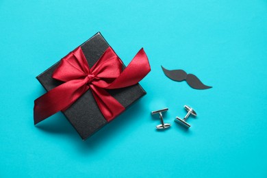 Photo of Gift box, cufflinks and paper mustache on light blue background, flat lay. Father's day celebration