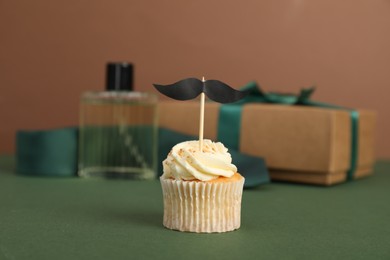 Photo of Happy Father's Day. Tasty cupcake with topper in front of presents on green table, closeup