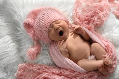Photo of Cute newborn baby in hat yawning on fuzzy blanket, top view