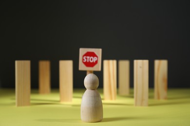 Photo of Overcoming barries for development and success. Wooden human figure in front of road Stop sign and blocks on yellow surface