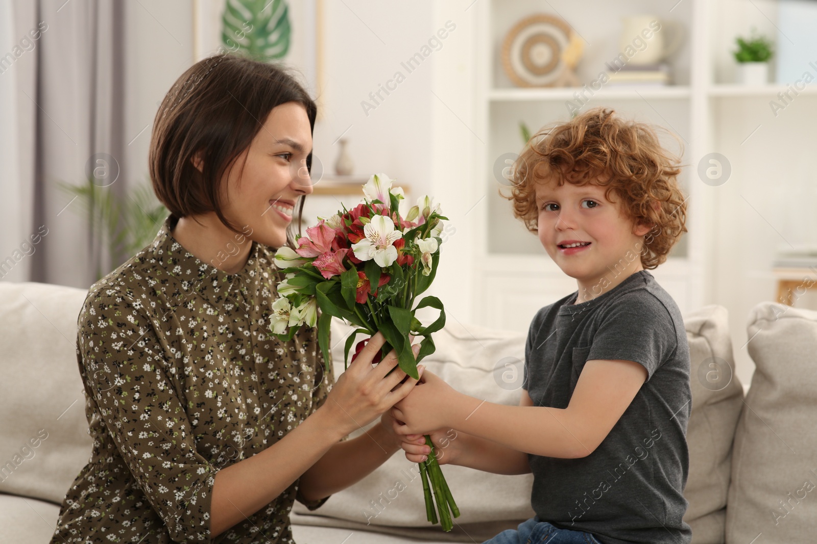 Photo of Happy woman with her cute son and bouquet of beautiful flowers at home. Mother's day celebration